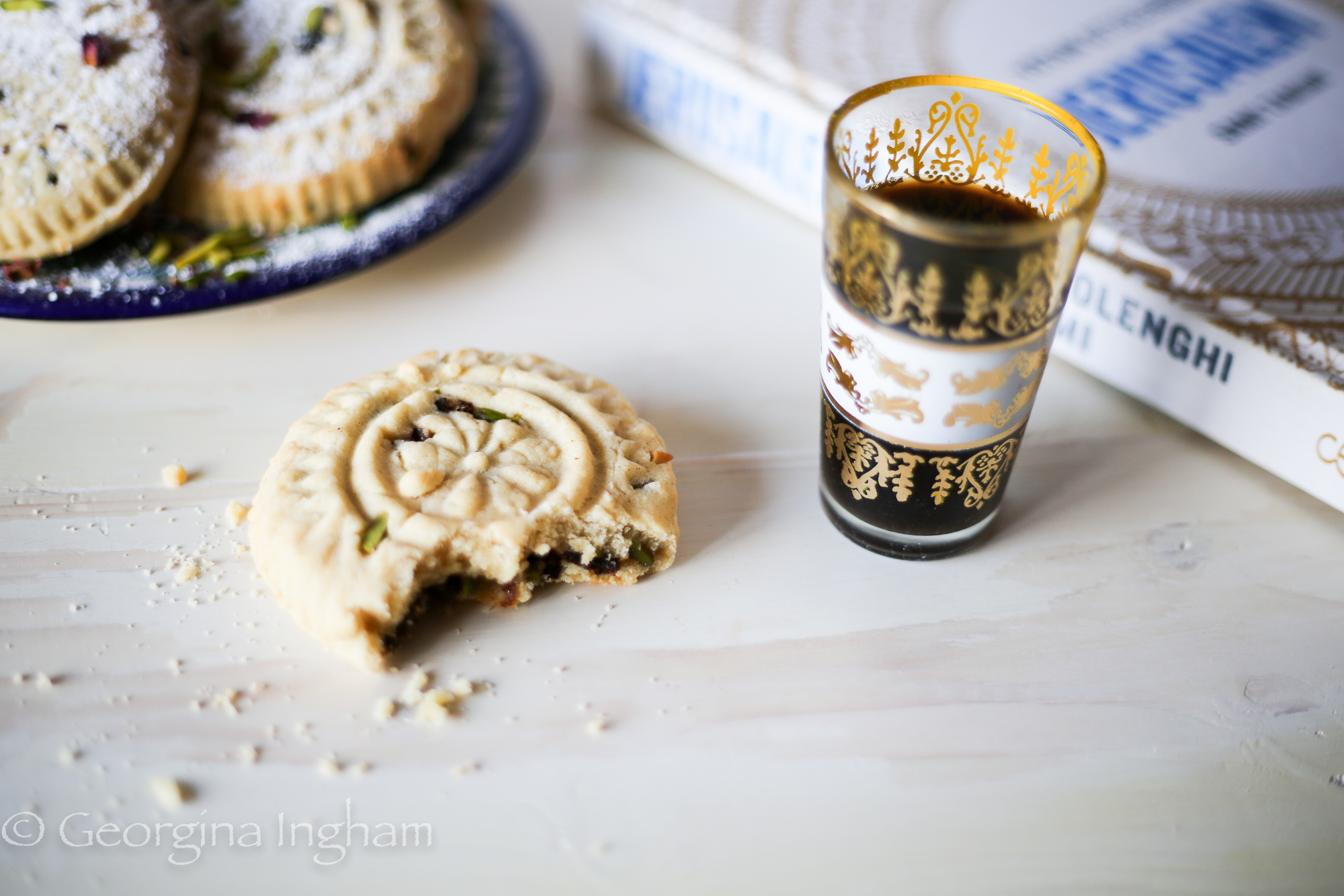 Bitten ma&rsquo;amoul cookie with date and pistachio filling served with Arabic coffee and the Jerusalem cookbook in the background